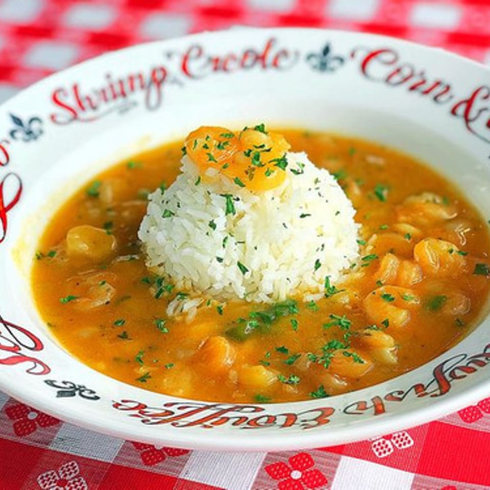 Shrimp Creole with white rice and parsley in a decorative bowl on a red and white checkered tablecloth.