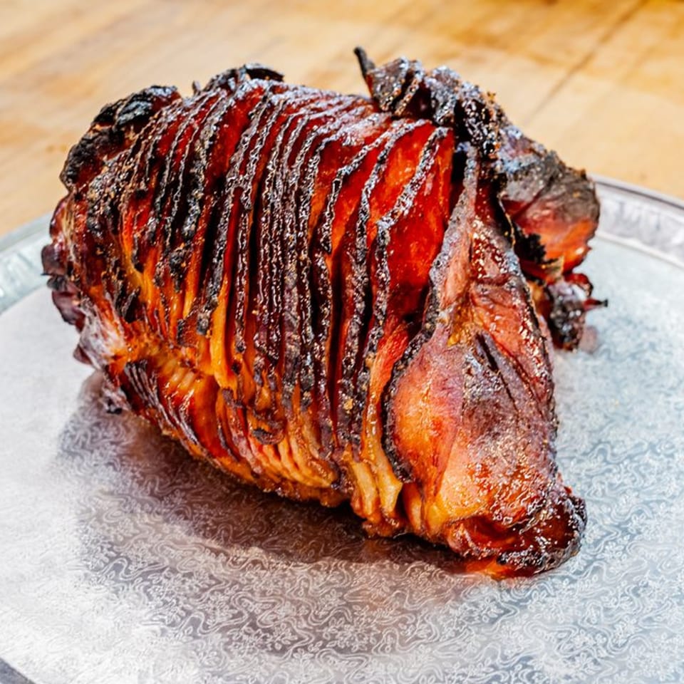A large, spiral-cut, glazed ham with a crispy, dark brown exterior on a silver platter.