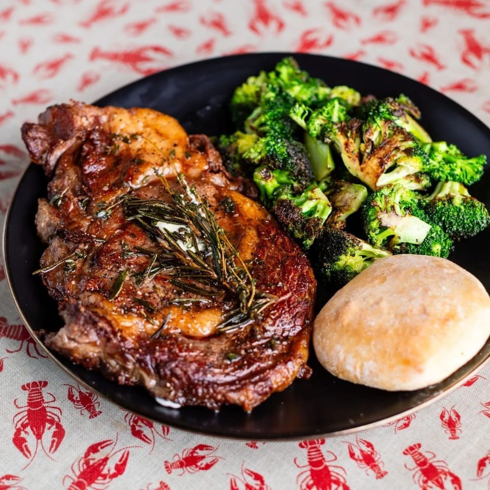 Taylor's Meat Company's BBQ steak with roasted broccoli, a bread roll, and rosemary garnish.